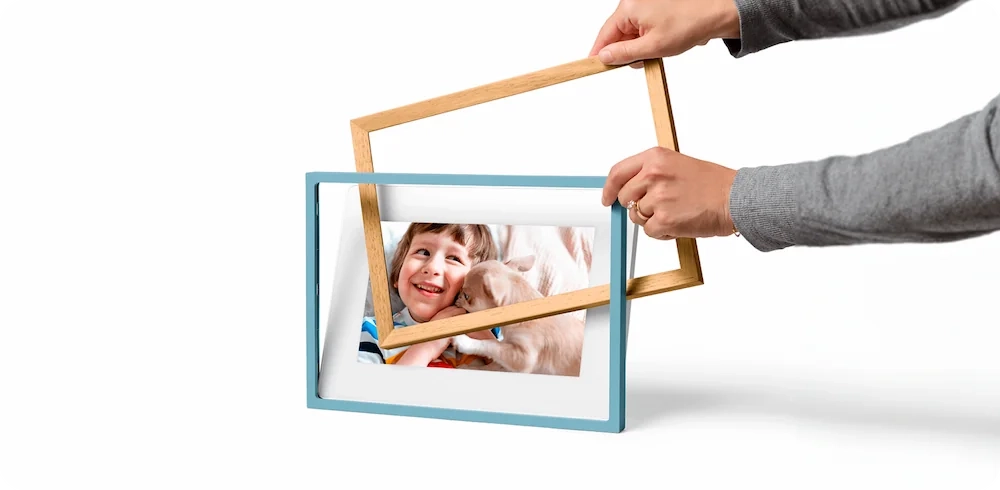 Hands swapping wooden frames on a digital display skylight frame 2 showing a child and dog photo, highlighting customizable frame options